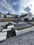 Gartenbaustelle mit modernen L-Steinen aus Beton, Trittplatten und einer dunklen Kiesfläche vor Wohnhäusern.