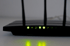 Schwarzer WLAN-Router mit drei Antennen und leuchtenden grünen Status-LEDs.