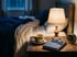 Kräutertee, Buch, Lesebrille und Wecker auf dem Nachttisch im warmen Licht einer Lampe