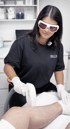 Eine Frau mit Schutzbrille führt eine Laser-Haarentfernung an einem Bein durch.