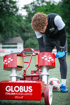 Fußballspieler bückt sich neben einer roten Ballmaschine mit "GLOBUS ITALIAN EXCELLENCE"-Logo und einem Fußball.