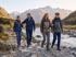 A family of four hiking along a dirt path next to a mountain lake and evergreen forest.