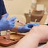 A healthcare professional in blue gloves administers a knee injection using a syringe filled with pink fluid.