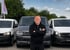 Mann mit gekreuzten Armen vor drei Lieferwagen, darunter ein dunkler VW Transporter.