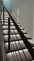 Moderne Holztreppe mit LED-Beleuchtung unter jeder Stufe und einem Geländer aus Holz und Metallstäben.
