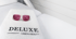 Rosa Schutzbrille auf einem weißen Handtuch mit schwarzem "DELUXE LASER & BEAUTY" Logo auf einer Behandlungsliege.