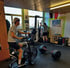 Zwei Männer trainieren in einem Fitnessstudio: Einer fährt ein Standfahrrad, der andere benutzt einen Stepper.