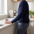 A man in a navy sweater stands at a white kitchen counter next to a coffee mug and an espresso machine.