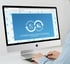 Eine Person tippt an einem iMac-Computer, der eine Website mit blauen Flammenmustern und zwei Kreissymbolen anzeigt.
