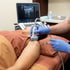 A clinician performs an ultrasound-guided shoulder injection on a patient using a transducer probe and a syringe.