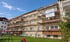 Eingerüstetes Mehrfamilienhaus mit Werbebanner von Gerüstbau Popaj vor blauem Himmel und einer Wiese mit Spielplatz.