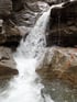 Ein tosender Wasserfall stürzt über graue Felsen in einen Bach mit einer orangefarbenen Schnur.
