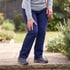 A person in navy pants and hiking shoes stands on a stone path, holding their knee in a garden setting.