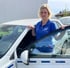Blonde Frau in blauem Polo-Shirt lehnt an offen stehender Tür eines weißen Autos.
