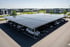 Solar-Carport über einem Parkplatz mit mehreren geparkten Autos und Gebäuden im Hintergrund.