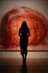 Silhouette einer Frau mit langen Haaren vor einem großen, abstrakten roten Gemälde.