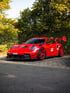 Roter Porsche 911 GT3 RS Manthey-Racing mit Heckflügel und roten Felgen parkt auf Asphalt.