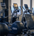 Mehrere Precor Crosstrainer und Fitnessgeräte stehen in einer Reihe vor einem Fenster im Fitnessstudio.