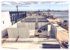 Bau einer großen grauen Betonstruktur an einem Hafen mit Kränen und Meer im Hintergrund.