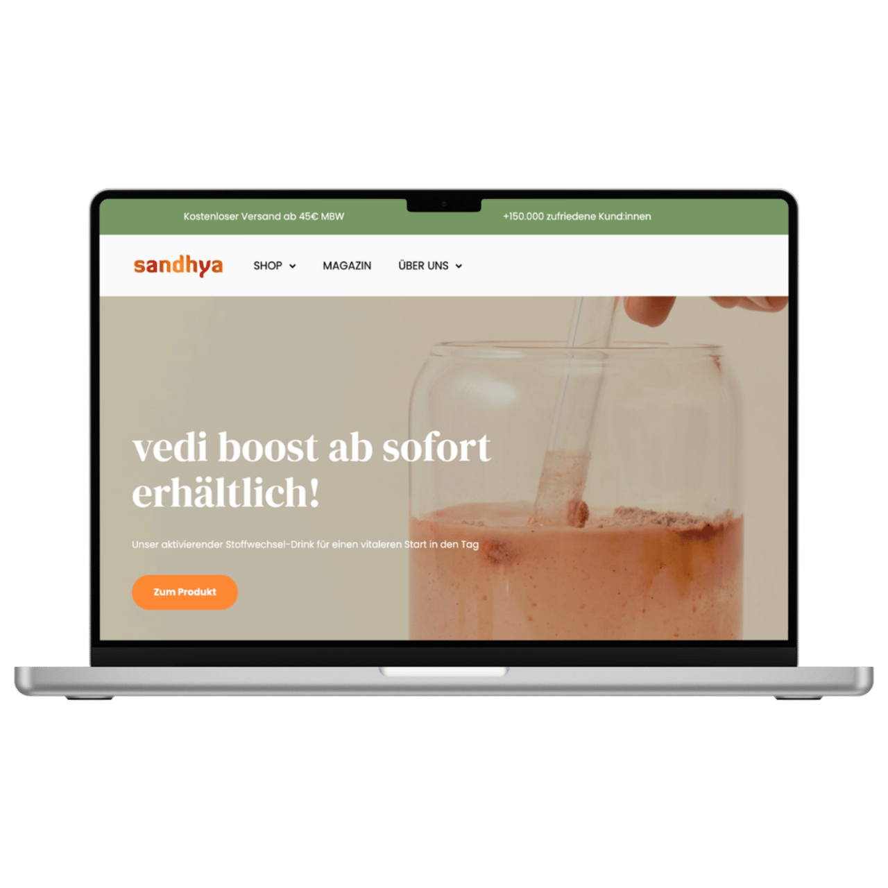 Ein silberner Laptop zeigt die Sandhya-Website mit dem Text vedi boost ab sofort erhältlich und einem Getränk.