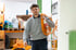 Junger Mann in grauer Sweatshirt trägt orangefarbenes Kabel mit Stecker über seiner Schulter in einer Lagerhalle.