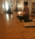 Menschen praktizieren Yoga-Übungen im Sitzen auf Matten in einem hellen Raum mit Holzboden im Vogthaus.