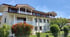Modernes frisch gestrichesnes Mehrfamilienhaus mit weißen Balkonen, Holzverkleidung im Dachgeschoss und Garten unter blauem Himmel.