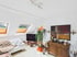 Helles Wohnzimmer mit Dachschrägen, weißem Sofa, Holzkommode, abstrakter Kunst und einer großen Zimmerpflanze.