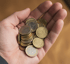 Eine Hand hält eine kleine Menge Euro-Münzen, darunter 1-Euro- und 20-Cent-Münzen.