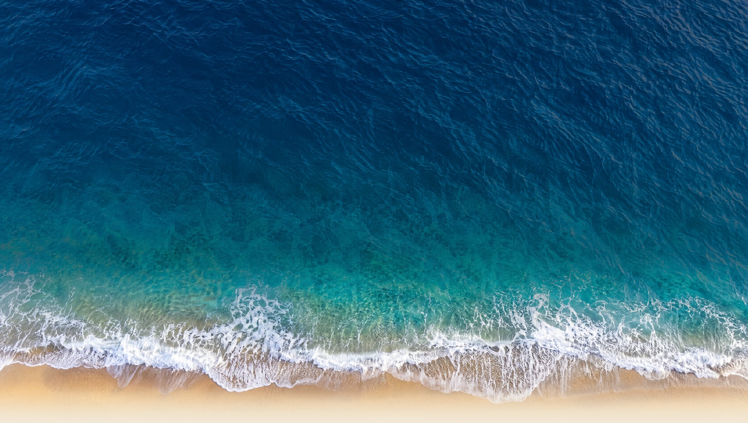 The sea seen from directly above, waves washing onto a sandy beach