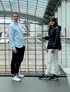 Mann und Frau stehen vor einer Glaswand mit Blick auf ein Flughafenvorfeld.