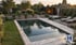 Moderner Garten mit Pool, Natursteinmauer, Saunahaus und Sonnenliegen bei Abenddämmerung von Hanischke GaLaBau.