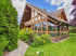Modernes Holzhaus mit großen Glasfronten, Wintergarten und gepflegtem Garten mit Steinweg unter blauem Himmel.