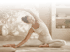 Frau in heller Sportkleidung dehnt sich in einer Yoga-Sitzposition mit seitlich ausgestrecktem Arm auf einer Matte.
