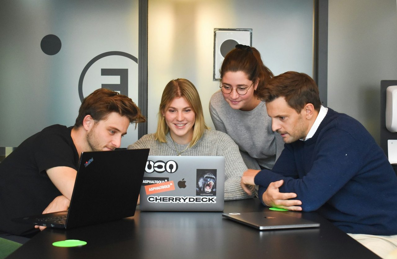 Vier Personen schauen in einem Besprechungsraum gemeinsam auf Laptops