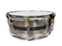 Snare-Drum aus gebürstetem Metall mit schwarzem Mittelstreifen, verchromten Spannböckchen und weißem Schlagfell vor schwarzem Hintergrund.