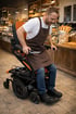 Mann im Rollstuhl mit brauner Schürze und Jeans in einer Bäckerei, fährt mit dem Rollstuhl.