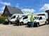 Drei Männer stehen vor drei weißen Lieferwagen mit grünen und schwarzen Logos.