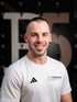 Lächelnder Physiotherapeut von Therapier im weißen Sportshirt mit Adidas-Logo vor dunklem Hintergrundund Pier5 
