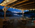 Holzterrasse mit Lichtern, Tischen und Stühlen vor einem Hafen bei Sonnenuntergang.