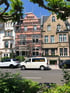 Rosa Gebäude mit Gerüst zwischen beigen und weißen Häusern, mit weißem Lieferwagen und SUV auf der Straße.