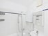Weiß gefliestes Badezimmer mit Badewanne, Duschwand aus Glas, Waschbecken und einem Spiegelschrank mit blauer Zierleiste.