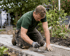 Gärtner in Arbeitskleidung kniet und glättet Pflastersteine auf einem Gartenweg.