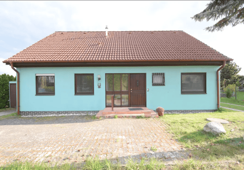 Türkisblaues Haus mit braunem Ziegeldach, gepflasterter Einfahrt und grüner Wiese.