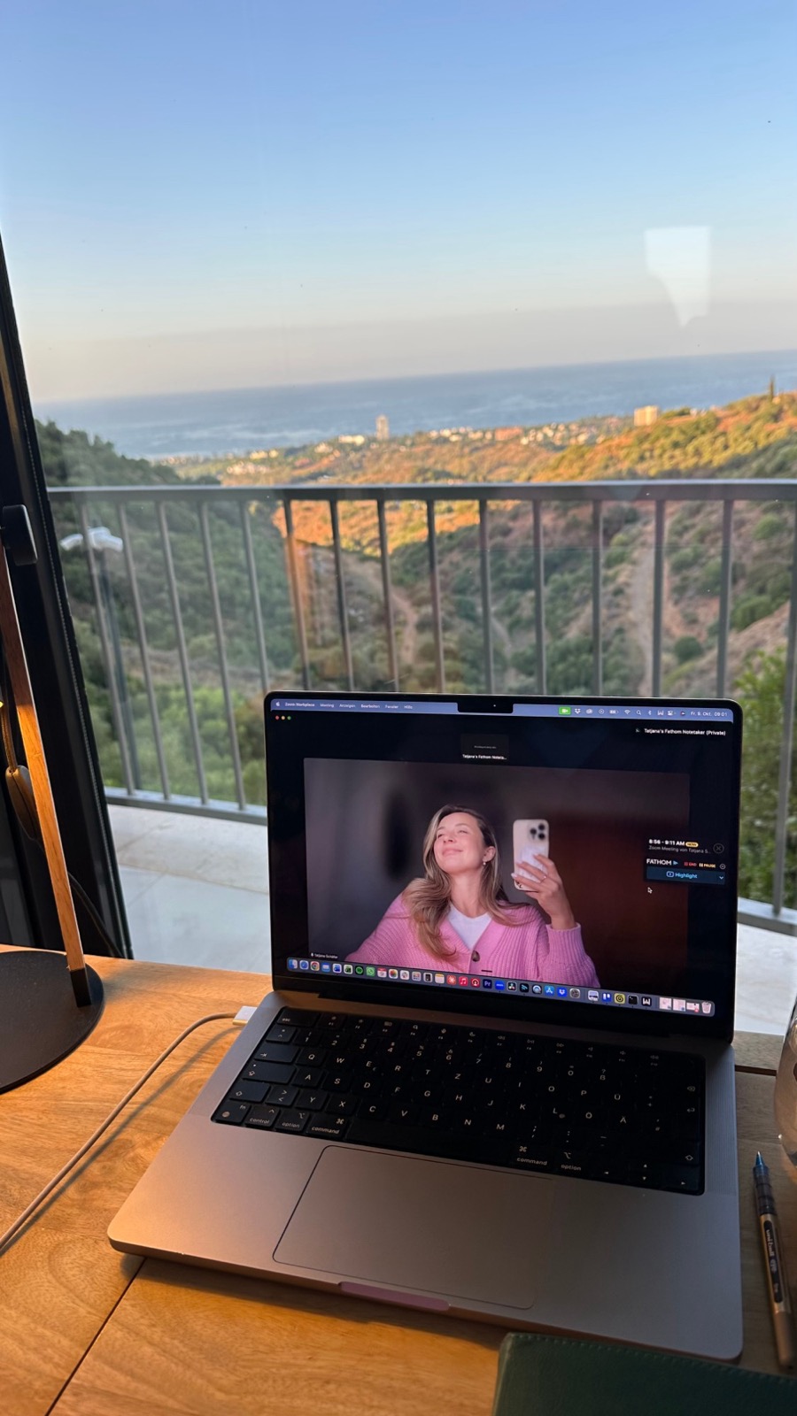 Laptop mit Videogespräch vor einem Fenster mit Blick auf Hügel und Meer