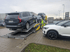 Ein grauer Volvo SUV wird auf einen Autotransporter geladen, daneben steht ein weißes Auto.