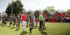 Fußballspieler und Schiedsrichter betreten den grünen Rasen des Spielfeldes, Fans mit roten und schwarzen Fahnen im Hintergrund.
