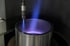 Ein blaues Plasma strömt aus einer Düse in einen zylindrischen Metallbehälter.