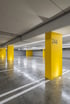 Leere, gut beleuchtete Tiefgarage mit leuchtend gelben Säulen und grauen Parkmarkierungen auf dem Betonboden.