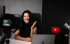 Frau mit langen dunklen Haaren filmt sich selbst am Schreibtisch, hinter ihr ein YouTube-Logo.